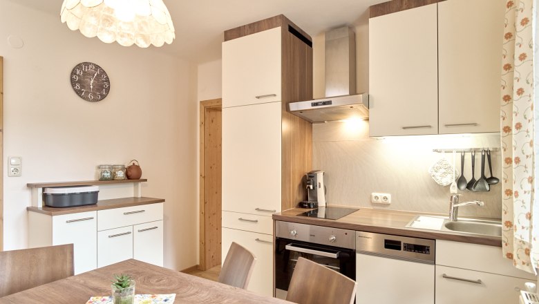 Moderne K&uuml;che mit Holz- und Wei&szlig;t&ouml;nen, Esstisch, H&auml;ngelampe und K&uuml;chenger&auml;ten.