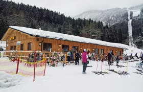 Skihütte im Schnee mit Skifahrern und Ausrüstung davor.