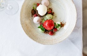 Ein Dessert mit verschiedenen Eiskugeln, Himbeeren und Minzblättern auf einem Teller.