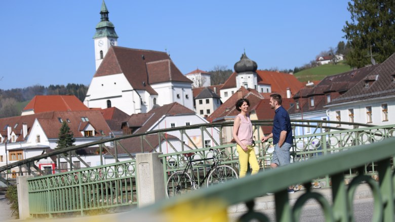 Ein Paar steht auf einer Brücke in Scheibbs mit einer Kirche im Hintergrund.