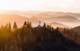 Die sanften H&uuml;gel des Mostviertels erstrahlen im warmen Licht des Herbstes, w&auml;hrend die B&auml;ume in leuchtenden Farben leuchten. Ein Kreuz auf dem Gipfel l&auml;dt Wanderer ein, die atemberaubende Aussicht auf die umliegenden Berge und T&auml;ler zu genie&szlig;en. Hier, wo die Natur in voller Pracht erbl&uuml;ht, findet jeder Besucher einen Ort der Ruhe und Inspiration.
