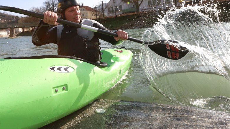 Person in grünem Kajak paddelt auf einem Fluss.