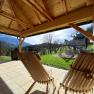 Blick aus einem Holzpavillon auf eine Berglandschaft mit Schaukel und Rutsche im Garten.