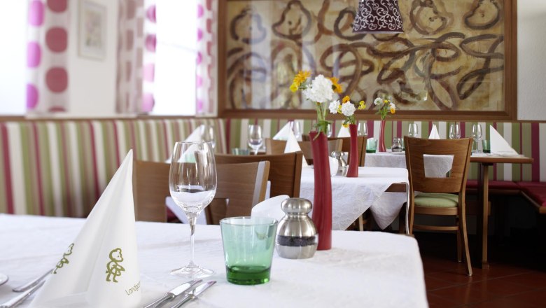 Innenansicht eines stilvoll gedeckten Restaurants mit weißen Tischdecken, Blumenvasen und Kunst an der Wand.