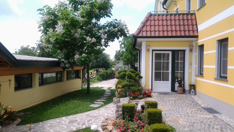 Eingang eines gelben Gebäudes mit gepflegtem Garten und gepflastertem Weg.