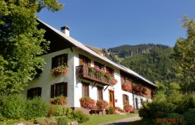 Ein traditionelles Haus mit Blumenkästen vor einem bewaldeten Berg.