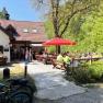 Eine Bergh&uuml;tte mit Terrasse, auf der Menschen an Tischen sitzen. Fahrr&auml;der sind im Vordergrund zu sehen, umgeben von gr&uuml;ner Natur.