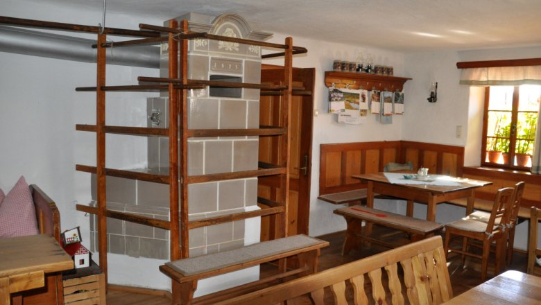 Innenansicht eines traditionellen Bauernhauses mit Kachelofen und Holzmöbeln.
