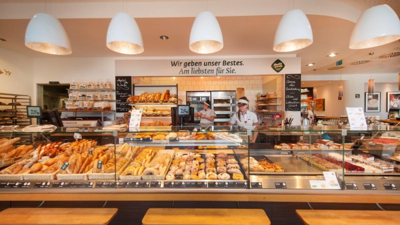 Innenansicht einer Bäckerei mit Theke voller Backwaren und zwei Angestellten.