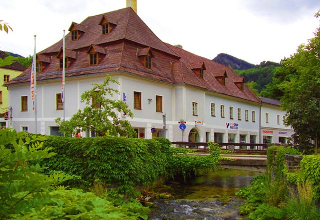 Pension Sun, © Pension Sun Historisches Gebäude mit rotem Dach an einem Bach, umgeben von grüner Vegetation.