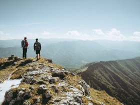 Zwei Wanderer stehen am Gipfel und genie&szlig;en den atemberaubenden Blick &uuml;ber die Ybbstaler Alpen. Die frische Bergluft und die majest&auml;tischen Landschaften laden dazu ein, die Seele baumeln zu lassen und die Sch&ouml;nheit der Natur zu erleben.