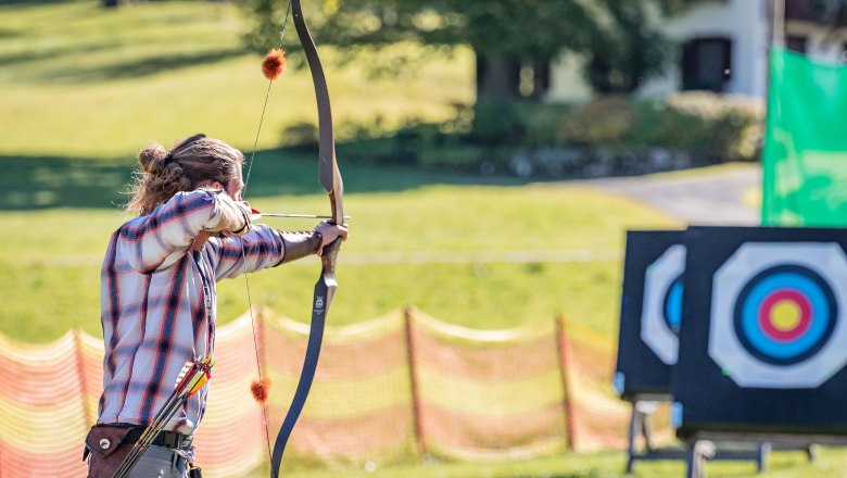 Mann h&auml;lt Pfeil und Bogen und zielt auf eine Scheibe.