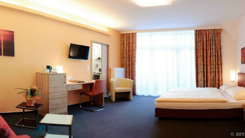 Modern eingerichtetes Hotelzimmer mit Doppelbett, Sofa, Schreibtisch und großem Fenster.