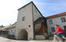 Ein historisches Gebäude mit einem Torbogen und einer Person auf einem Fahrrad im Vordergrund.