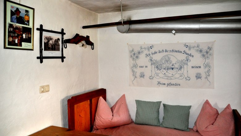 Innenansicht eines traditionellen Zimmers mit Holzmöbeln, Kissen und Wanddekorationen im Bauernhausmuseum Ablass.