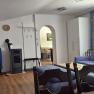 Gem&uuml;tliches Wohnzimmer einer Ferienwohnung mit blauen Sofas, Holzm&ouml;beln und einem Kamin. Ein Esstisch ist im Hintergrund sichtbar.