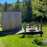 Eine kleine Holzh&uuml;tte mit Terrasse und Tisch im Gr&uuml;nen, umgeben von B&auml;umen, direkt am Teich gelegen.