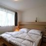 Modern eingerichtetes Schlafzimmer mit Doppelbett, hellem Holzmobiliar und großen Fenstern mit weißen Vorhängen.