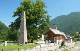 Historisches Gebäude mit Schornstein und Wasserrad in ländlicher Umgebung.