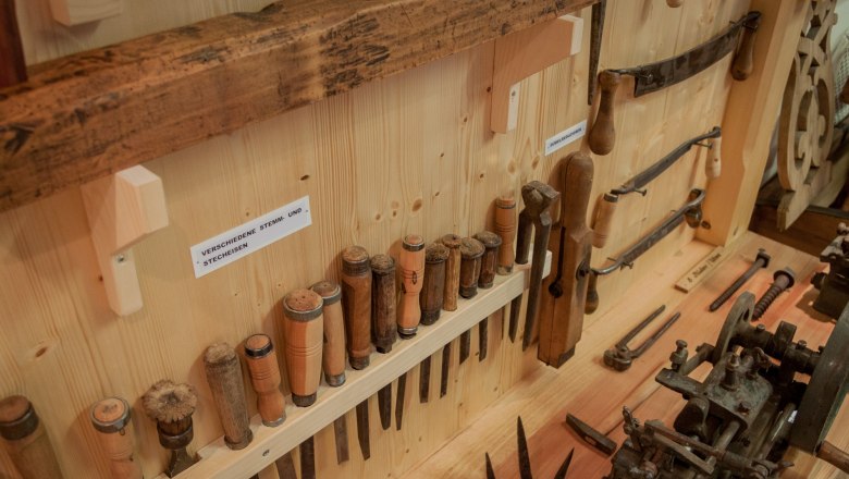 Eine Sammlung von Holzwerkzeugen, darunter Stemm- und Stecheisen, an einer Holzwand ausgestellt.
