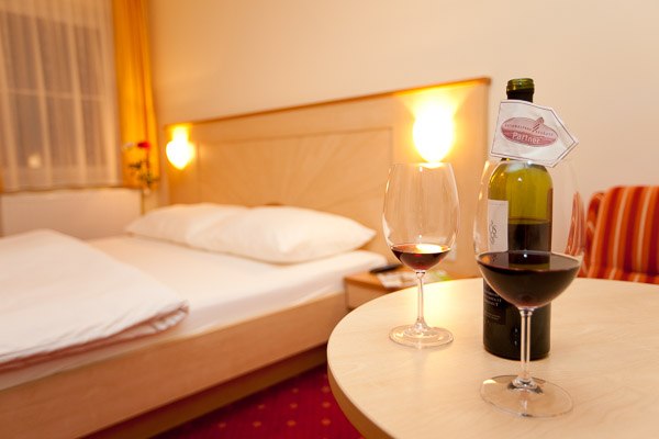 Ein gemütliches Hotelzimmer mit einem Doppelbett, zwei Weingläsern und einer Weinflasche auf einem Tisch.
