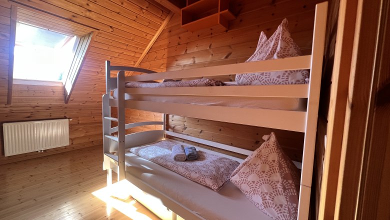 Ein gem&uuml;tliches Schlafzimmer mit Holzverkleidung und einem Etagenbett unter einem Dachfenster.