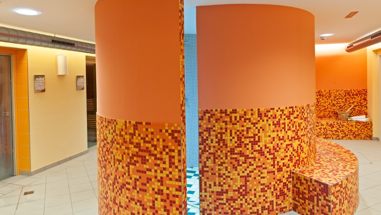 Innenansicht eines Wellnessbereichs mit orangefarbenen Mosaikfliesen und runden Wänden.