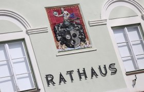 Fassade eines Rathauses mit dekorativem Wappen und Schriftzug 'Rathaus'.