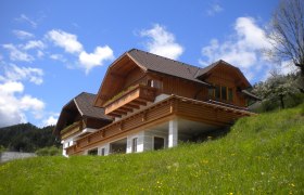 Ein traditionelles Holzhaus auf einem gr&uuml;nen H&uuml;gel unter blauem Himmel.
