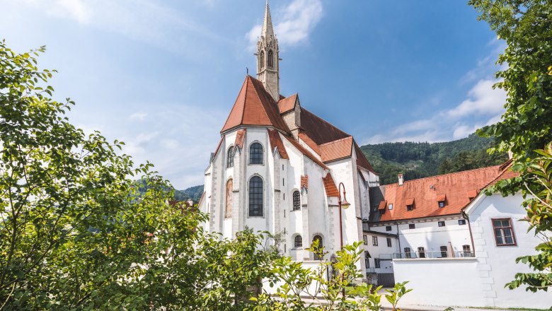 Historisches Gebäude mit rotem Dach und Turm, umgeben von Bäumen.