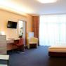 Modern eingerichtetes Hotelzimmer mit Doppelbett, Sofa, Schreibtisch und gro&szlig;em Fenster.