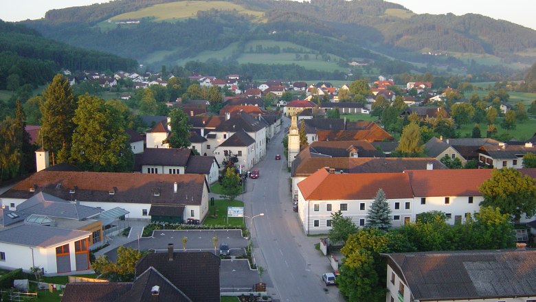 Luftaufnahme eines Dorfes mit roten Dächern und grüner Landschaft im Hintergrund.