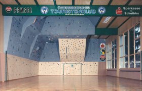Innenansicht einer Kletterhalle mit blauer Kletterwand und bunten Griffen.