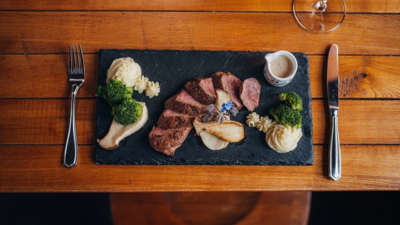 Gourmetgericht auf Schieferplatte mit Fleisch, P&uuml;ree, Brokkoli und So&szlig;e.