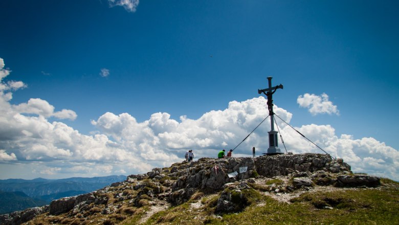 Gipfelkreuz auf dem Dürrenstein mit Wanderern und Wolken am Himmel.