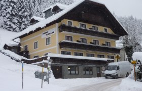 Ein verschneites Gebäude mit der Aufschrift 'Pension Panorama' in einer winterlichen Landschaft.