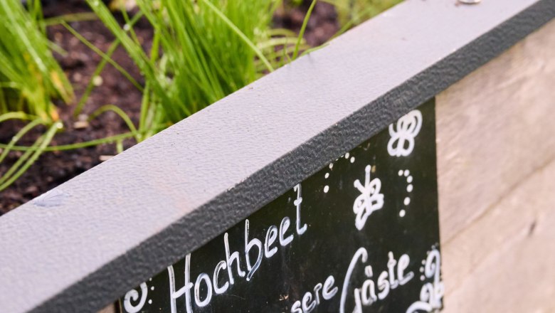 Ein Hochbeet mit Kr&auml;utern und einem Schild mit der Aufschrift 'Hochbeet f&uuml;r unsere G&auml;ste'.