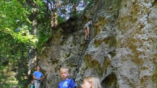 Kinder klettern an einer Felswand im Wald.