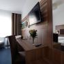 Modern eingerichtetes Hotelzimmer mit Doppelbett, Schreibtisch, Flachbildfernseher und Blumenstrauß.