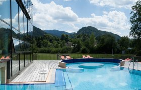 Au&szlig;enbereich des Ybbstaler Solebads mit Pool und Liegest&uuml;hlen, umgeben von gr&uuml;nen H&uuml;geln und B&auml;umen.