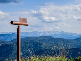 Die majest&auml;tischen Gipfel des Gro&szlig;en &Ouml;tschers erheben sich stolz gegen den klaren Himmel, w&auml;hrend die sanften H&uuml;gel und bl&uuml;henden Wiesen eine einladende Kulisse f&uuml;r Wanderer bieten. Ein Fernrohr l&auml;dt dazu ein, die atemberaubende Aussicht zu genie&szlig;en und die Sch&ouml;nheit der Natur in vollen Z&uuml;gen zu erleben.