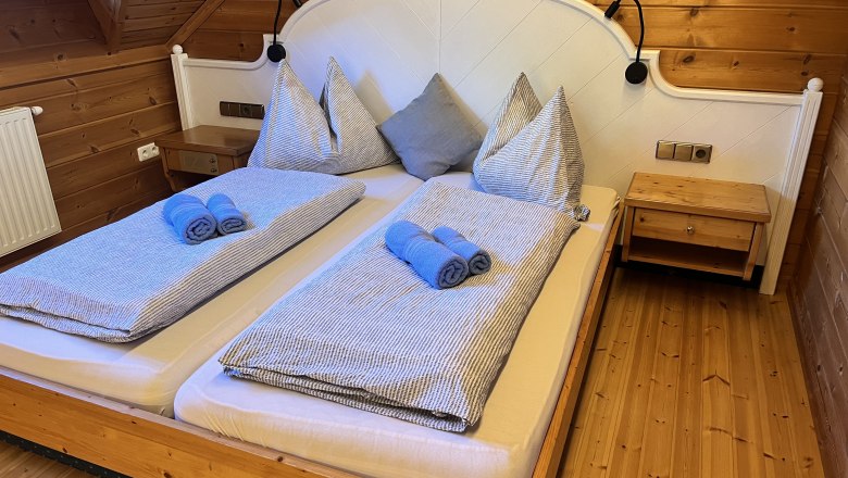 Gem&uuml;tliches Schlafzimmer mit Holzw&auml;nden und einem Doppelbett, das mit blauen Handt&uuml;chern und gestreifter Bettw&auml;sche dekoriert ist.