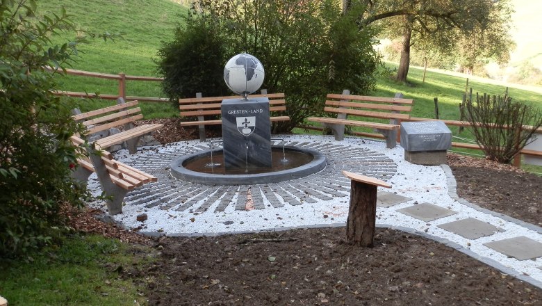 Ein Rastplatz mit Bänken und einem Meridianstein in einer ländlichen Umgebung.