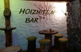 Rustikale Bar mit Holzmöbeln und Schriftzug 'Hoizhitt'n Bar' an der Wand.