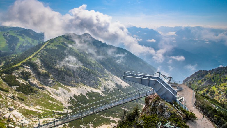 Aussichtsplattform auf einem Berg mit Wolken und grüner Landschaft.