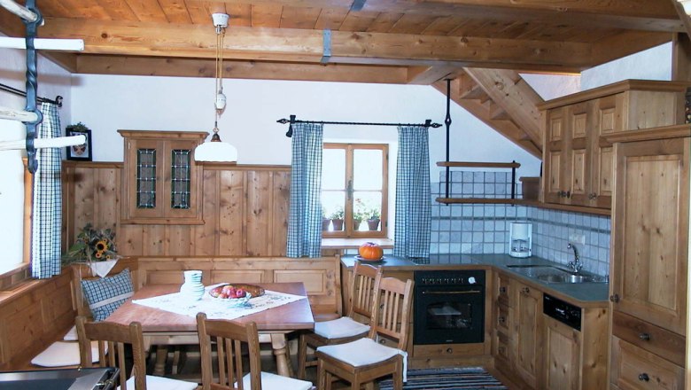 Rustikale Küche mit Holzmöbeln, Esstisch und Stühlen, Herd, Spüle und Fenster mit karierten Vorhängen.