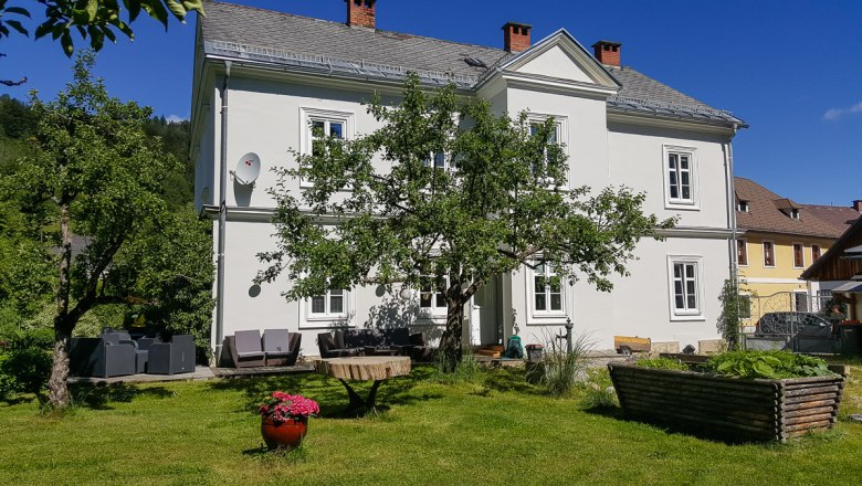 Ein wei&szlig;es zweist&ouml;ckiges Haus mit Garten und B&auml;umen.