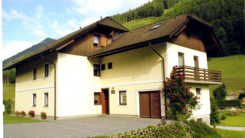 Fam. Kupfer, © Brigitte Kupfer Ein zweistöckiges Haus mit Balkon und Rosenstrauch, umgeben von grünen Hügeln.