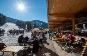 Menschen sitzen im Freien vor einem Restaurant in einem Skigebiet.