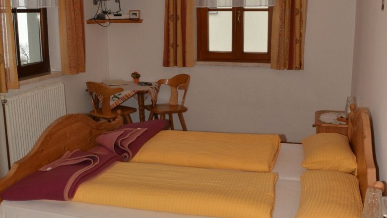 Gemütliches Schlafzimmer mit Doppelbett, Holzmöbeln und kleinem Tisch mit Stühlen.